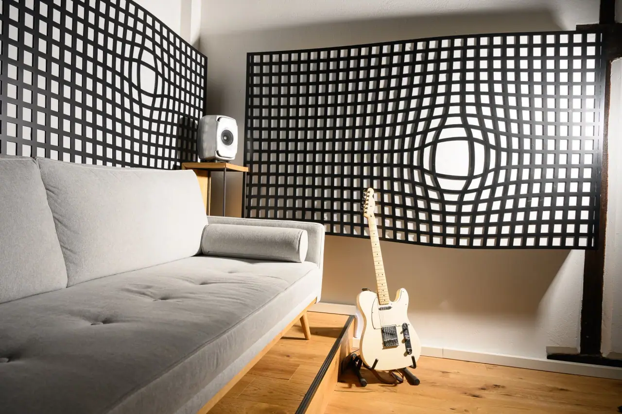 Lounge corner of the studio with a sofa, an electric guitar and black diffusor panels.