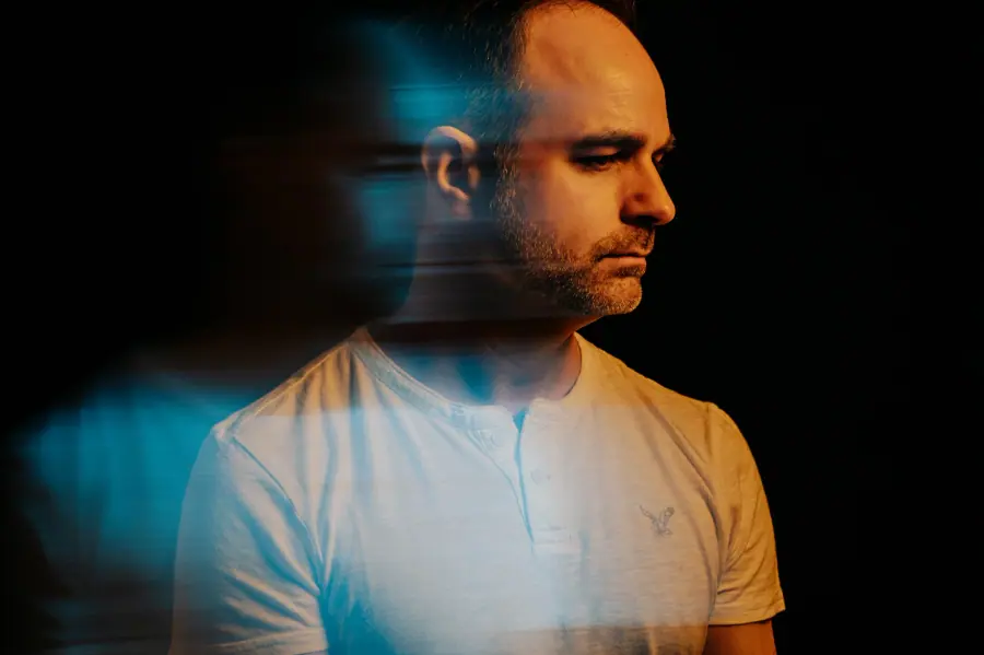 Portrait of Thomas Lemmer in blue and orange stage light.
